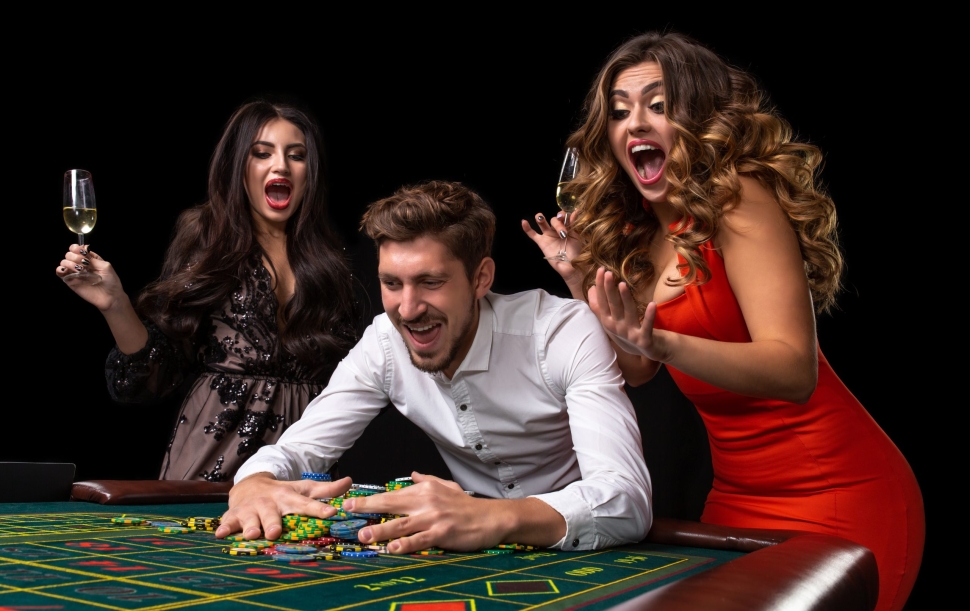 Adult group celebrating friend winning at roulette. Roulette table in a casino. Black background